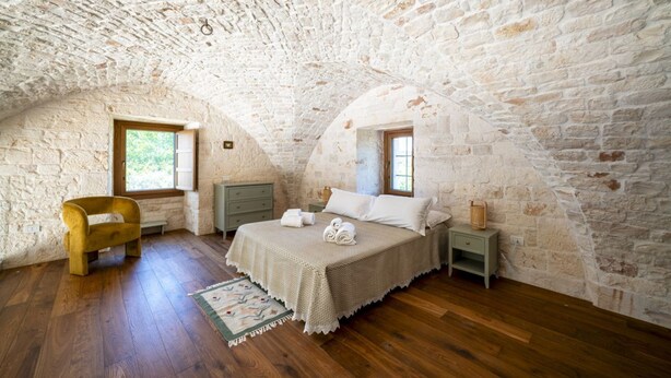 A bedroom with a stone ceiling, wooden floor, a bed with white linens, a wooden chair, and a nightstand with a lamp. - Palmento Giorgio: historic countryside retreat in the Itria Valley (Martina Franca)