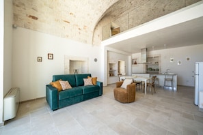 A spacious living area with a sofa, a chair, a dining table, and a kitchen in the background. - Palmento Giorgio: historic countryside retreat in the Itria Valley (Martina Franca)