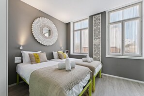 Un dormitorio moderno con dos camas, un espejo decorativo y ventanas amplias.