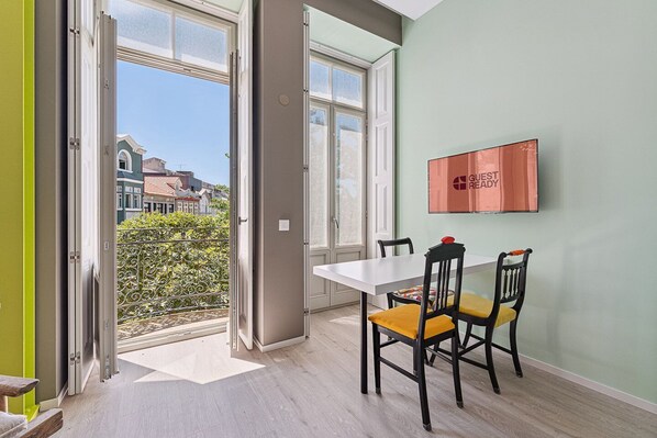 Una habitación con una mesa de comedor, dos sillas, un ventanal con vistas a edificios y un cartel en la pared.
