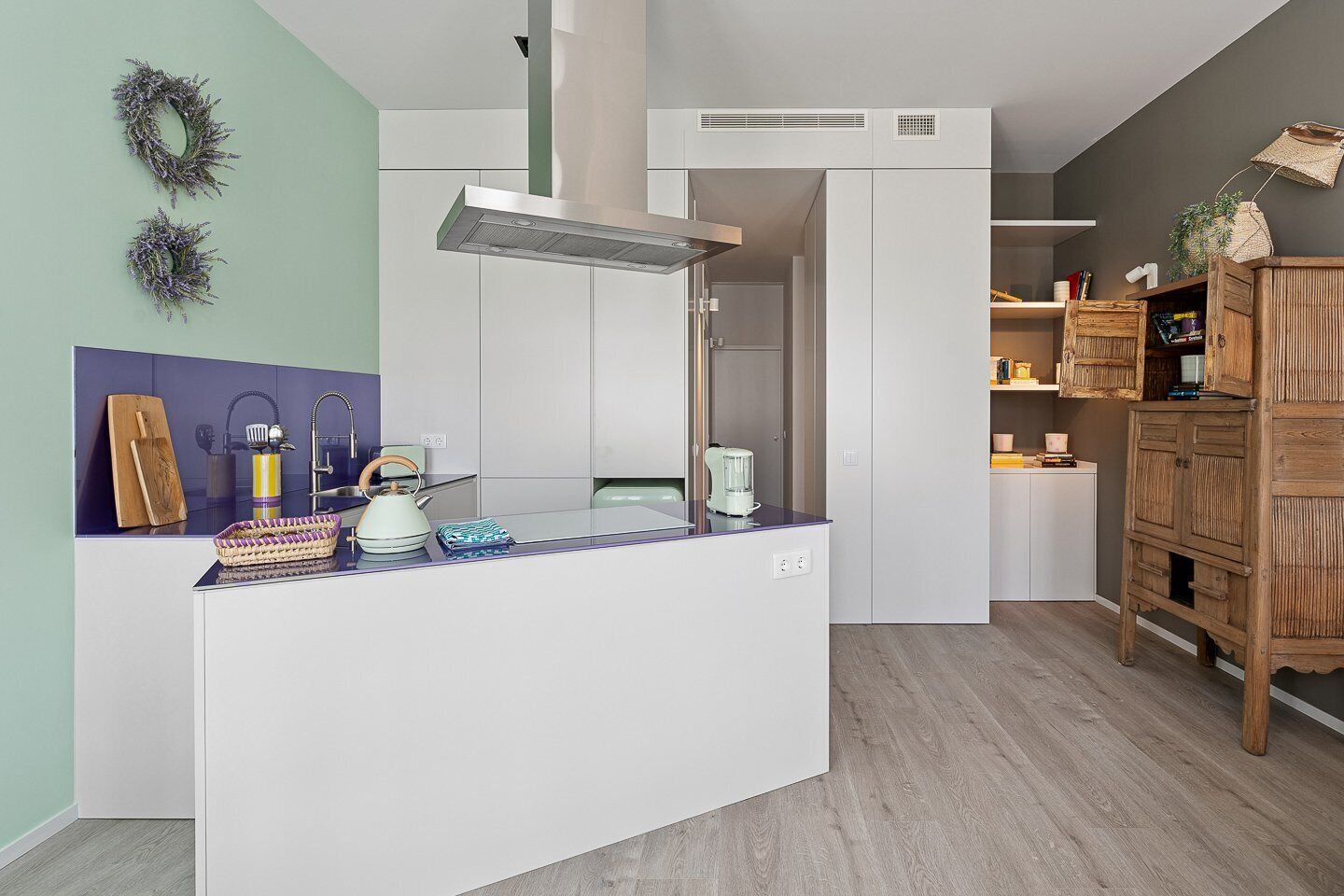 Una cocina moderna con una isla central, armarios blancos y un mueble de madera con espacio de almacenamiento.