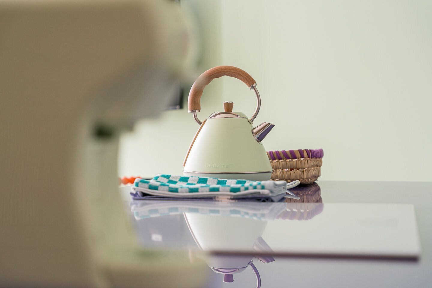 A kitchen area with a kettle, a basket, and a cloth on a reflective surface.