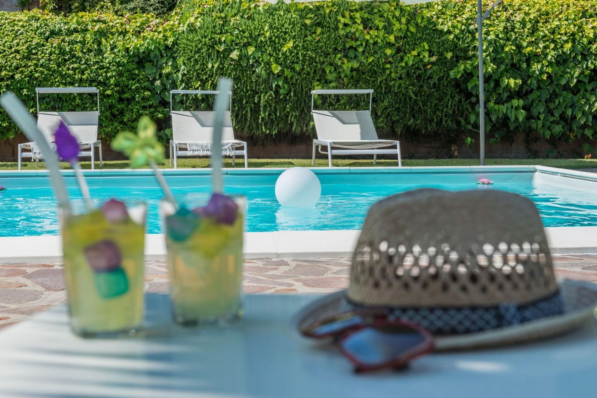 Escena junto a la piscina con sillones de descanso, un sombrero y bebidas.