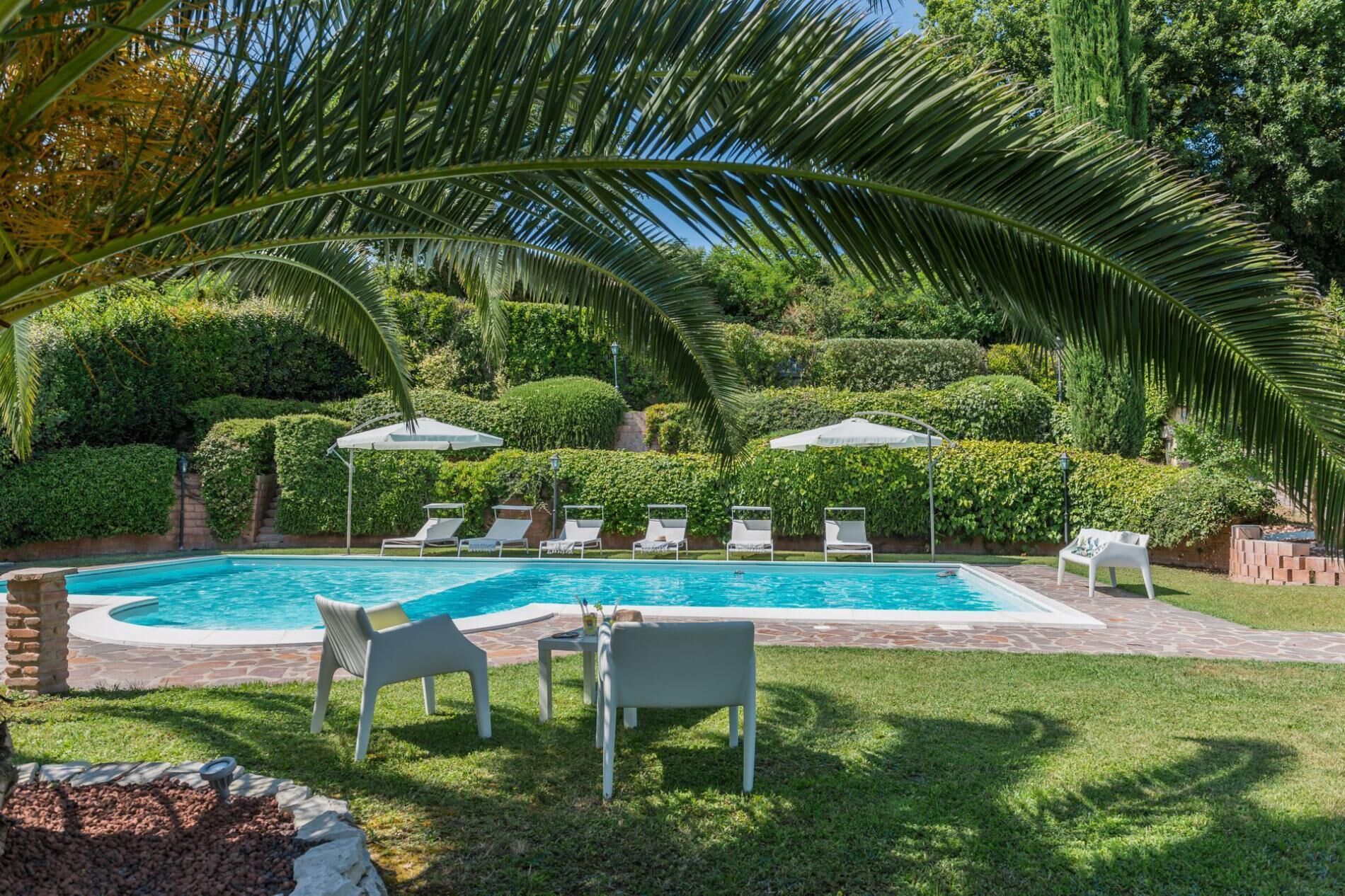 A swimming pool with lounge chairs and umbrellas, surrounded by lush greenery and palm trees.