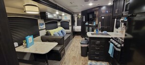 A compact kitchen with a dining area, a small trash bin, and a sofa with cushions.