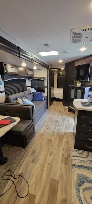 A compact RV interior with a kitchenette, a seating area with cushions, and a small table.