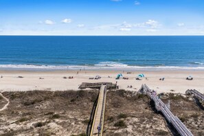 Ein Strand mit einer Holzpromenade, die zum Wasser führt, feinem Sand und einem klaren, blauen Himmel.