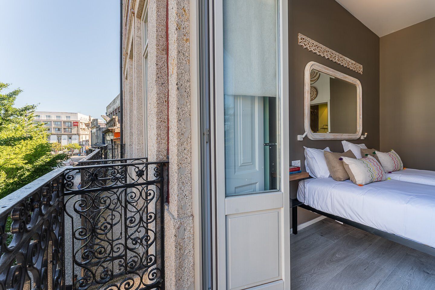 Une chambre à coucher avec un lit, un grand miroir et un balcon doté d’une balustrade en fer forgé.