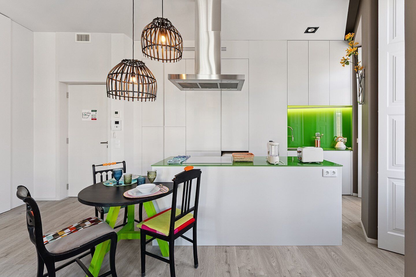 A modern kitchen with a central island, pendant lights, and a green accent wall.