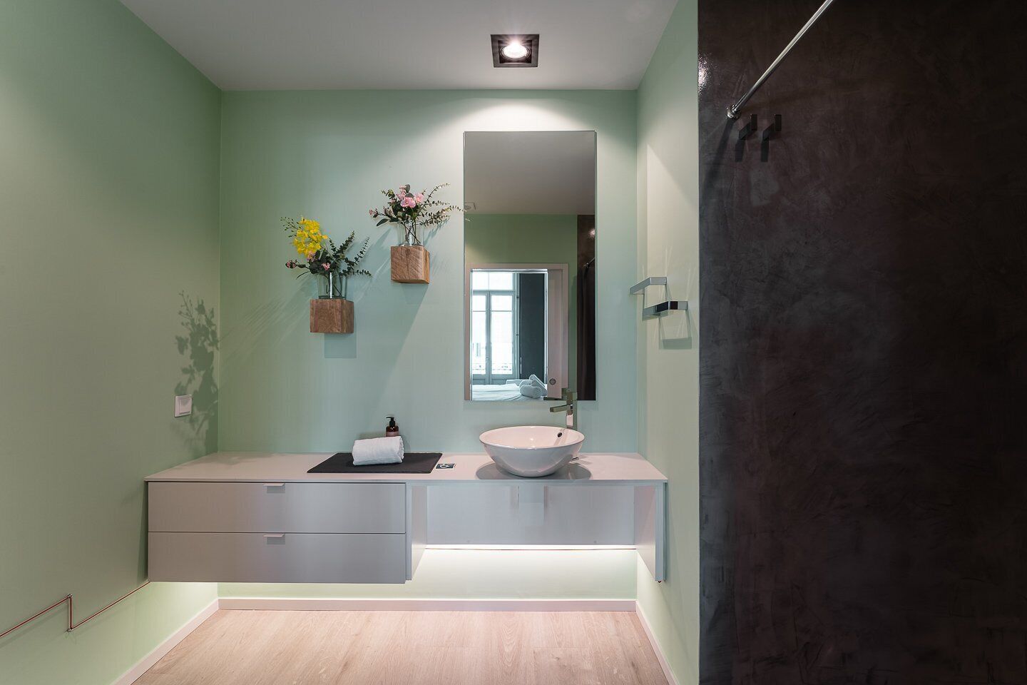 Une salle de bain moderne avec un grand miroir, un lavabo rond et un espace douche aux couleurs sombres.