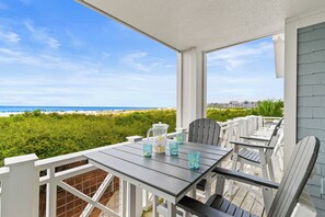 A covered outdoor seating area with a table and chairs, overlooking a beach and ocean.
