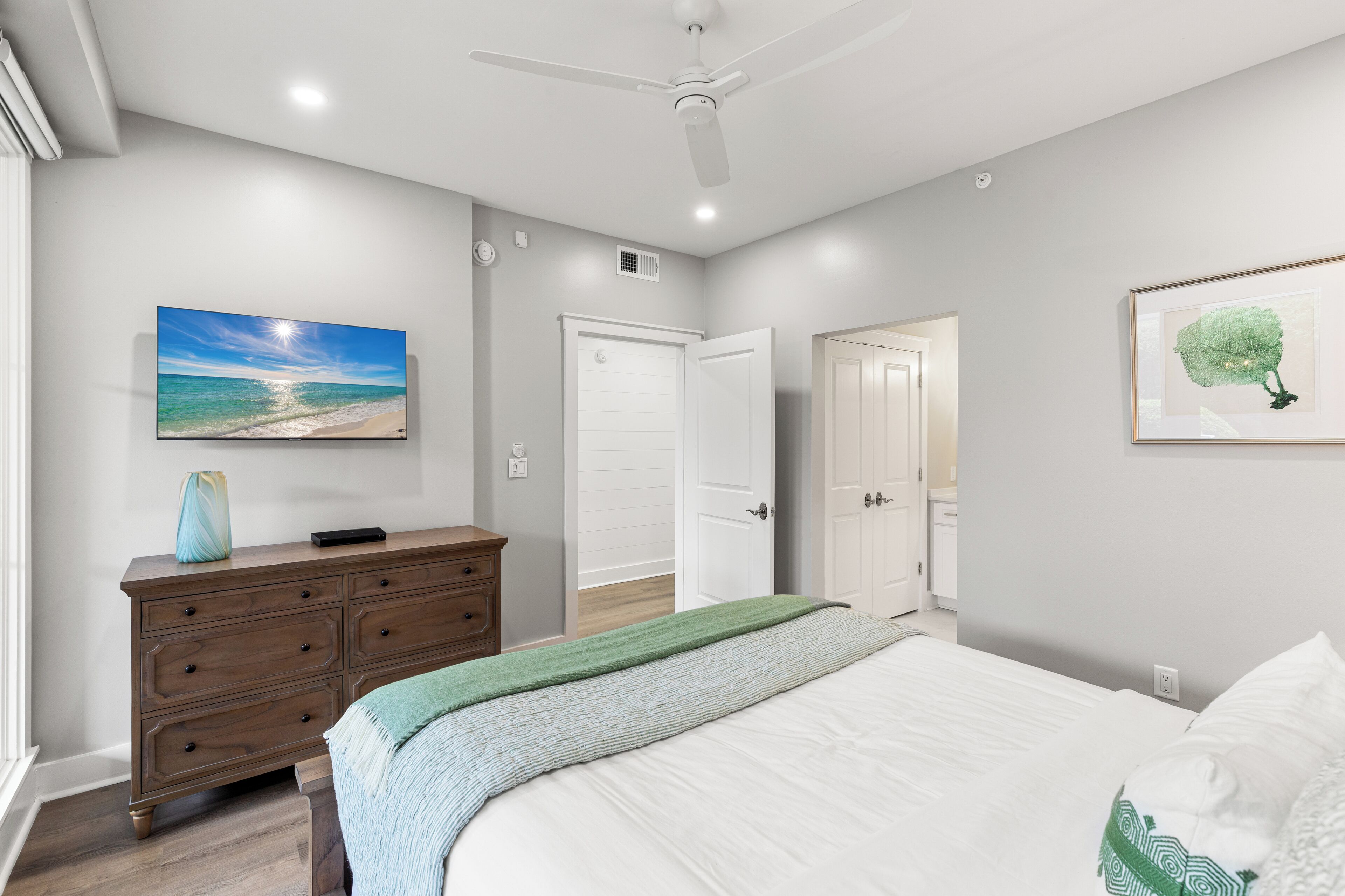 A bedroom with a bed, dresser, ceiling fan, and artwork on the walls.