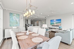 A modern living room with a wooden dining table, white sofas, and a large TV. - Community Pool, Luxury! Gulf Front, Watersound (Santa Rosa Beach)