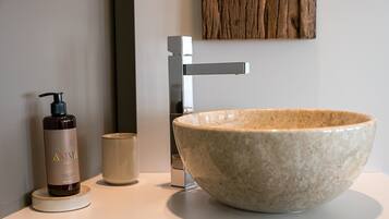 A bathroom with a large ceramic sink, a modern faucet, a bottle of shampoo, and a small cup.