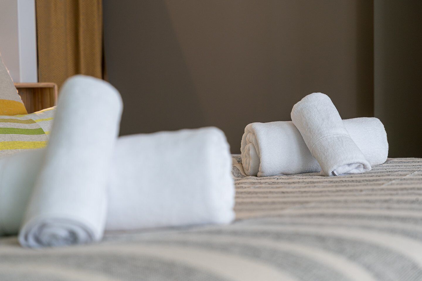A neatly made bed with rolled white towels and a striped blanket.