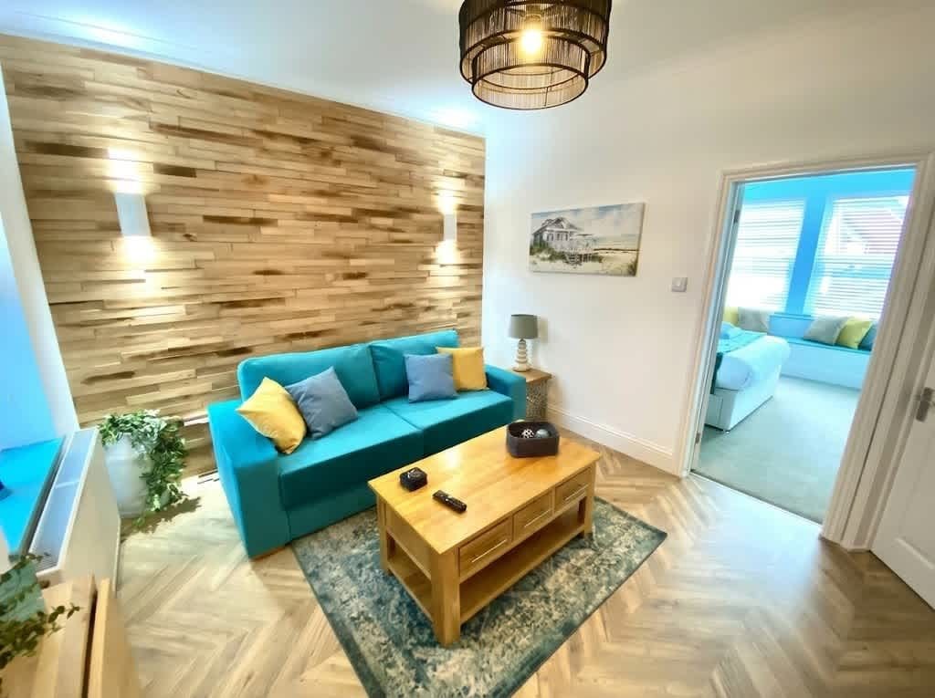 Een woonkamer met een houten wand, een blauwe bank, een bijzettafeltje en een uitzicht door een deur.