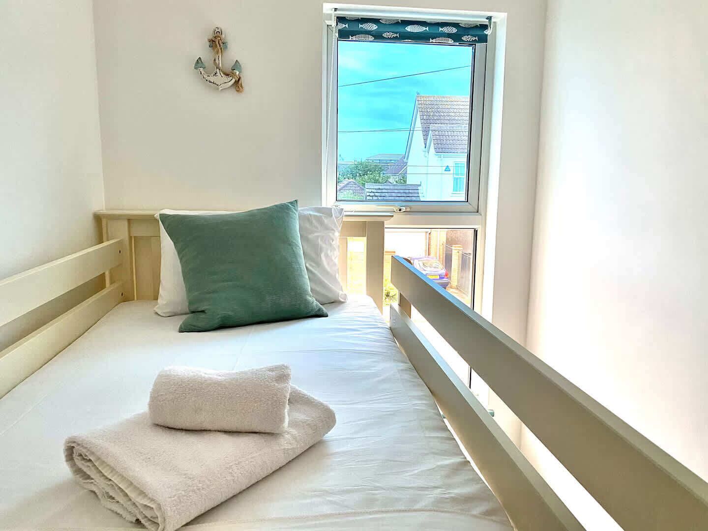 A small, single-bed room with a window overlooking a residential area.