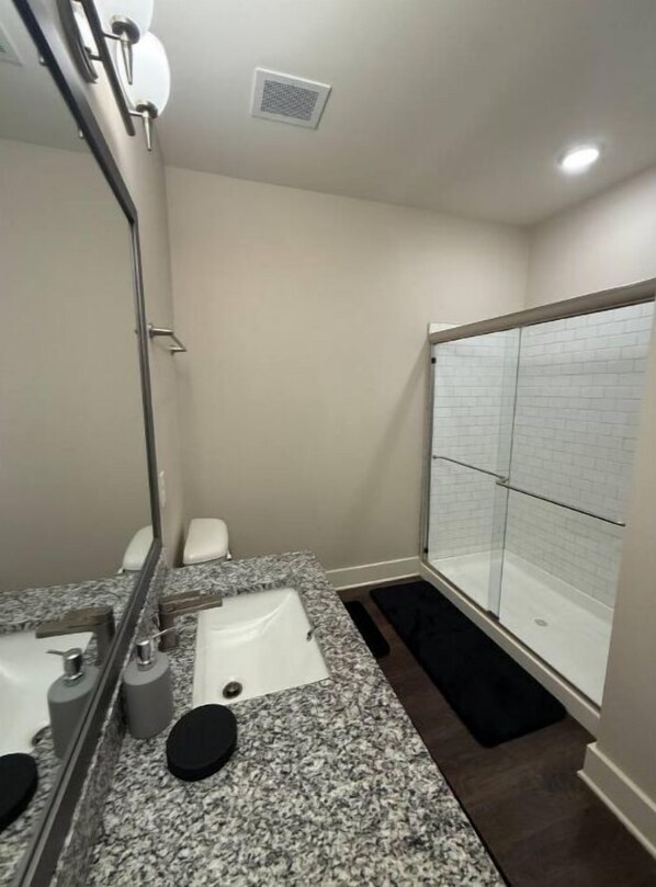 Un baño pequeño con encimera de granito, un espejo, inodoro y zona de ducha.