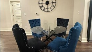 A dining area with a round glass table, four upholstered chairs, and a wall-mounted clock. - Luxurious Plush Apartment (McDonough)