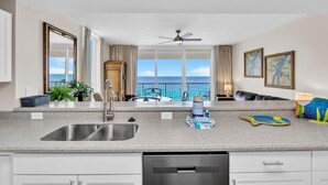 A modern kitchen with a large island, a built-in dishwasher, and a view of the ocean. - Majestic Beach Towers 1-715 (Panama City Beach)