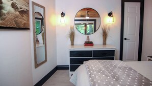 A bedroom with a bed, a dresser, two wall-mounted mirrors, and a door.