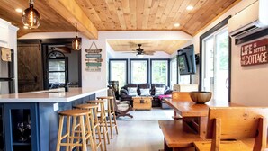 A cozy kitchen with wooden bar stools, a dining table, and a large window.