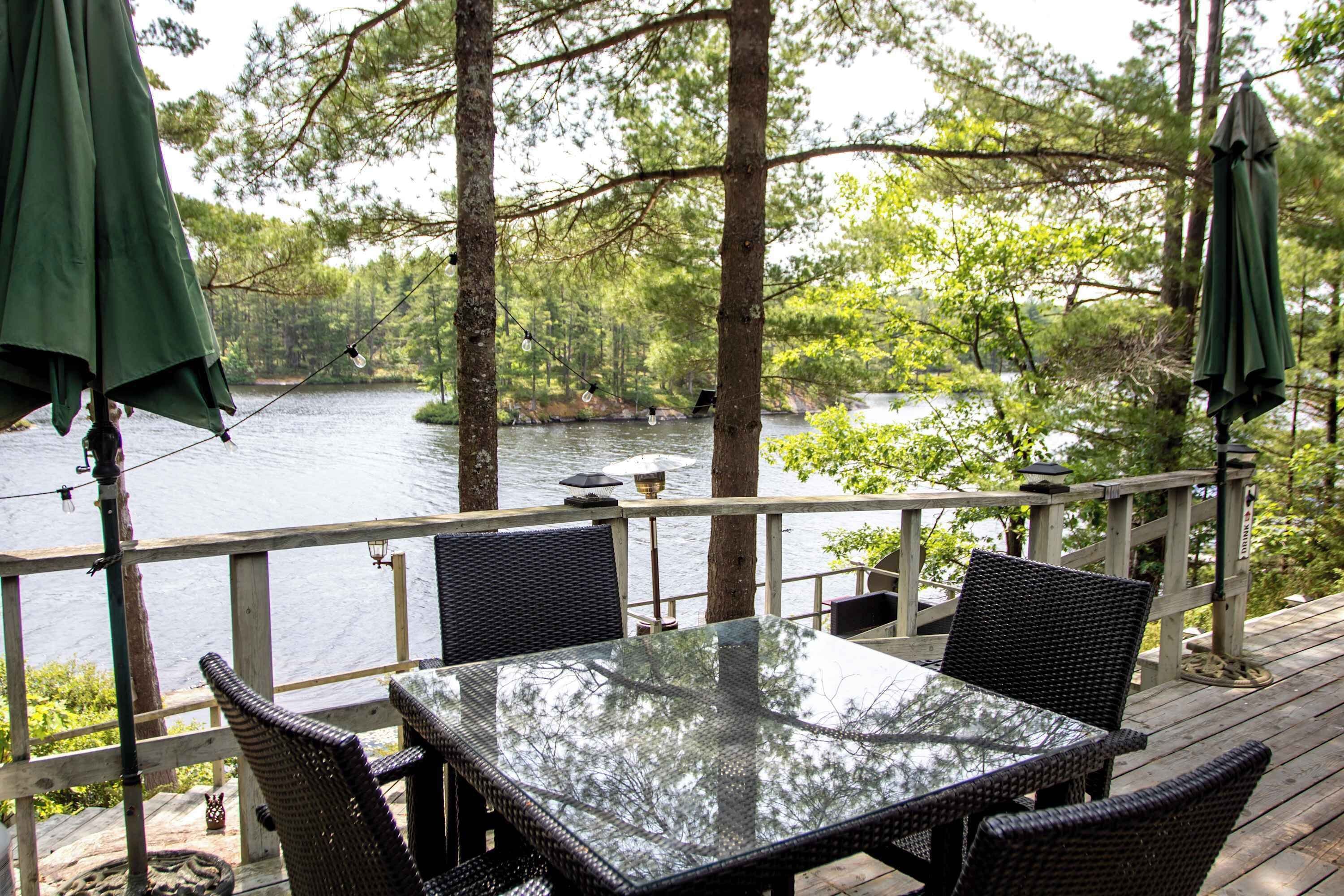 Um terraço com mesa e cadeiras, dando vista para um lago, rodeado por árvores.