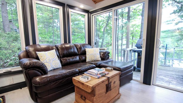 A leather sofa with patterned cushions, a wooden chest of drawers, and a view of a deck with outdoor furniture.