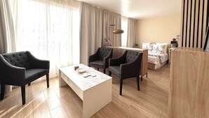 A modern hotel room with a large window, a sofa, two armchairs, a coffee table, and a bed with a wooden headboard. - Studio with beautiful view of the Eiffel Tower, 10 minutes' walk from the Champs-de-Mars (Paris)