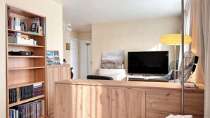 A modern living room with a wooden bookshelf, a flat-screen TV, a sofa, and a lamp. - Studio with beautiful view of the Eiffel Tower, 10 minutes' walk from the Champs-de-Mars (Paris)