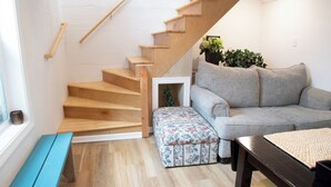 Een modern interieur met een houten trap, een grijze bank, een houten bankje en een kleine tafel.