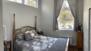 A bedroom with a wooden bed, a nightstand, a window with curtains, and a radiator.