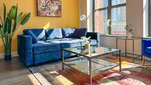 A modern living room with a blue sofa, a glass coffee table, and a colorful rug.