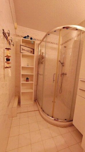 A small, enclosed shower area with a glass door, a shelf with various items, and a tiled floor.