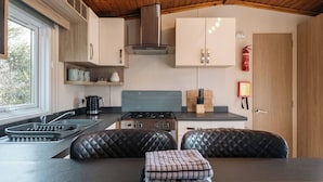 A modern kitchen with a gas stove, a range hood, and a window. There are two black leather chairs and a table with a cloth.
