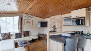 A modern living room with a sofa, a coffee table, and a TV. There is a kitchen area with a microwave and a toaster.