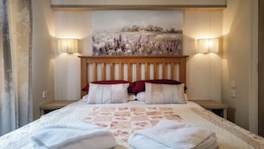 A neatly made bed with a floral quilt, two red pillows, and two white pillows. There are two wall-mounted lamps on either side of the bed.