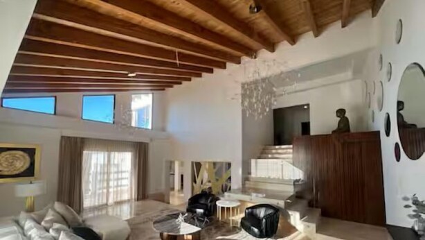 Amplia sala de estar con techo alto, un sofá grande, una mesa de centro y una escalera que sube a un nivel superior.