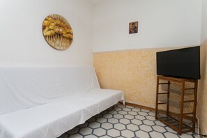 A white sofa, a round wall decoration, a television on a stand, and a patterned floor. - M048 – Marcelli, three-room apartment with sea view and garden (Marcelli)