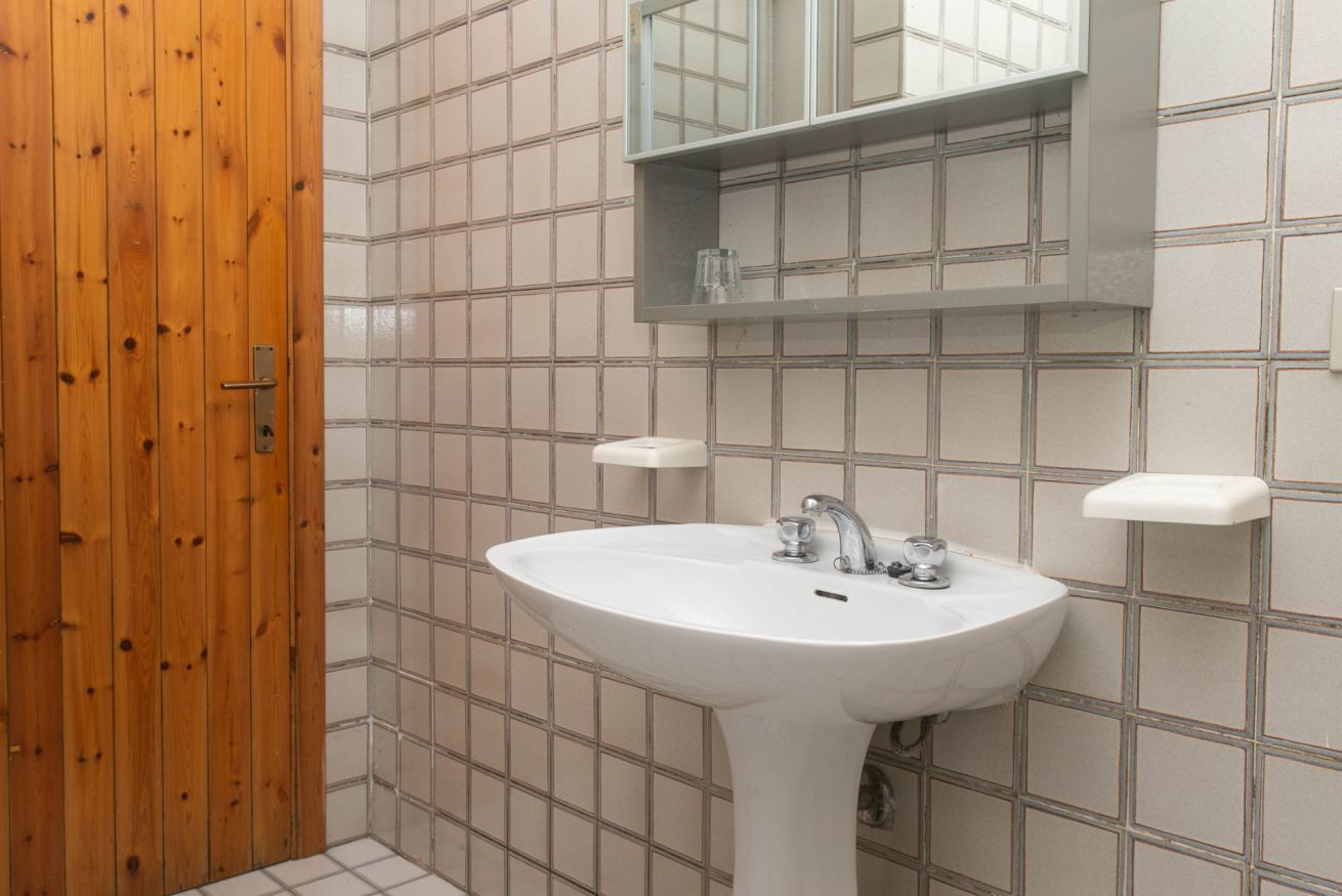 A bathroom with a wooden door, a white sink, and a mirror above it.