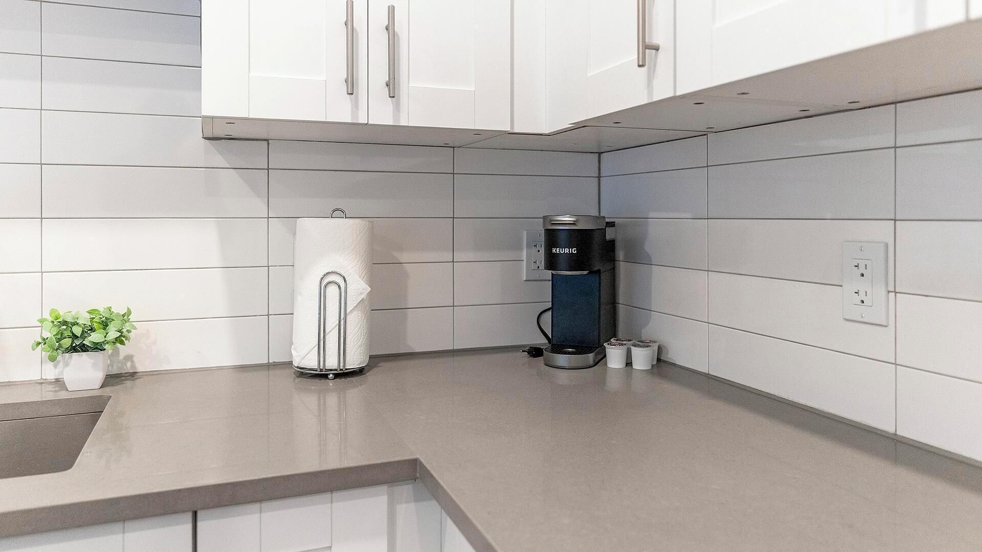Una cucina moderna con mobili bianchi, una macchina per il caffè e una piccola pianta in vaso.