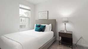 A bedroom with a bed, pillows, a nightstand, a lamp, a window, and a wall-mounted picture. - Landing | Incredible 3BD, Gym (Davenport)