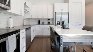 Una cocina moderna con armarios blancos, un refrigerador de acero inoxidable y una isla central con taburetes de bar.
