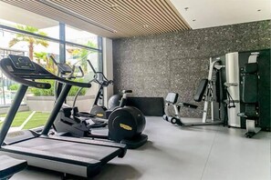A modern gym with cardio machines, weightlifting equipment, and a large window providing a view of the outdoors.