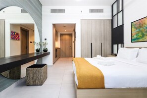 A modern hotel room with a large bed, a bedside table, a mirror, and a view into the hallway.