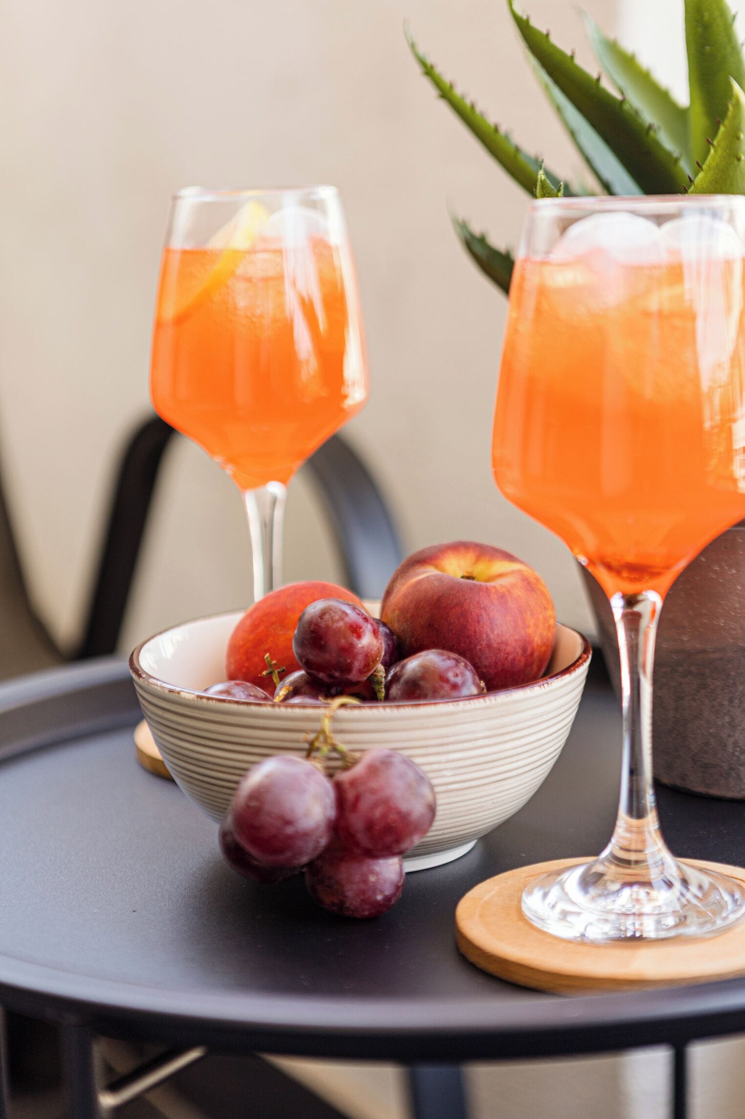 Deux verres d’une boisson à l’orange, un saladier de fruits et un aloe vera en pot, le tout posé sur une table.