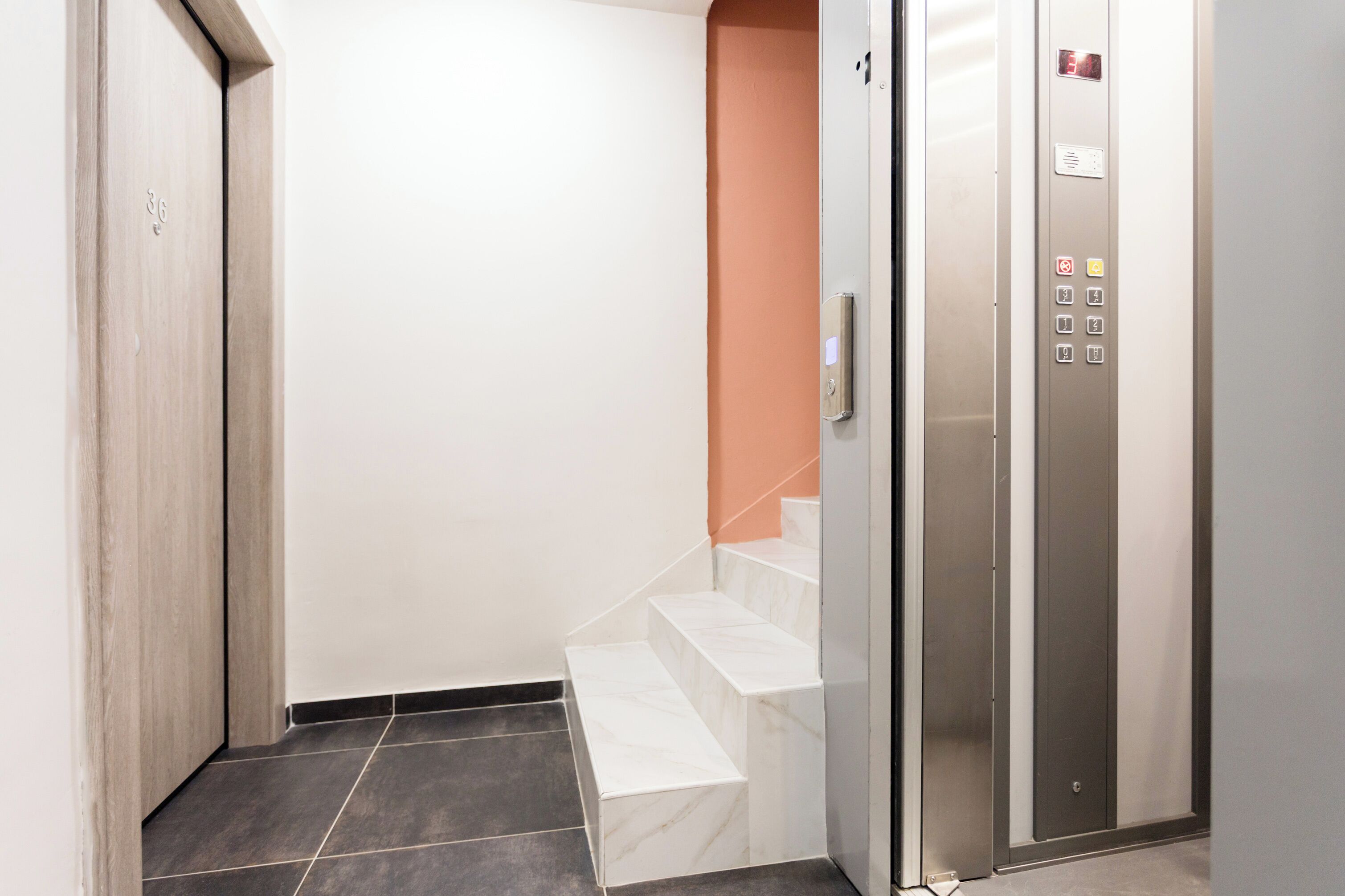 An elevator with a control panel, a marble staircase, and a door with a number.