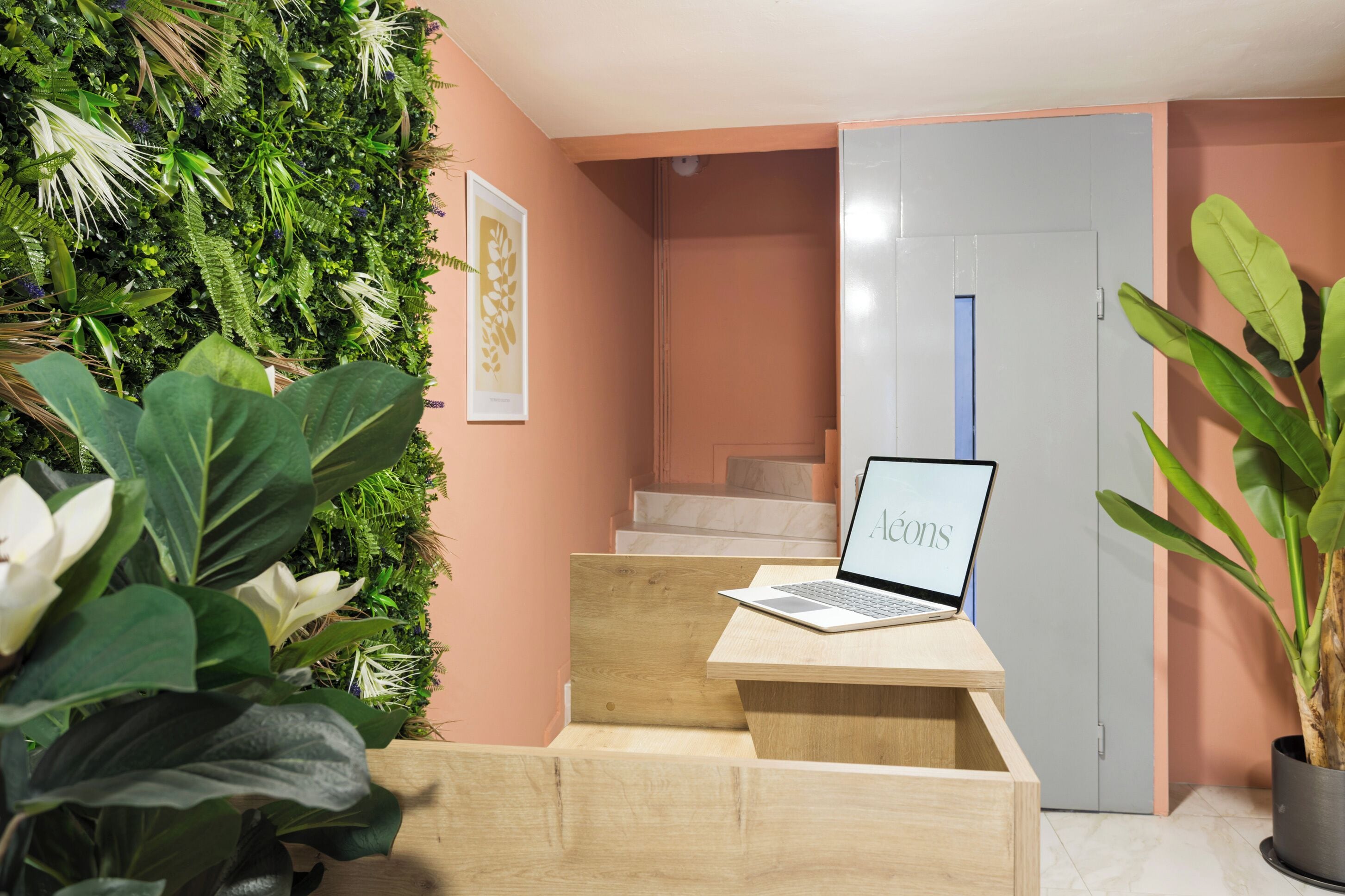 A modern interior with a laptop on a wooden desk, a staircase, and a green wall with plants.
