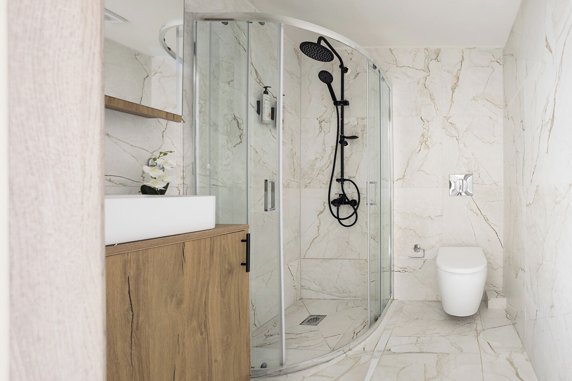 A modern bathroom with a glass-enclosed shower, a wooden vanity, a white sink, and a toilet.