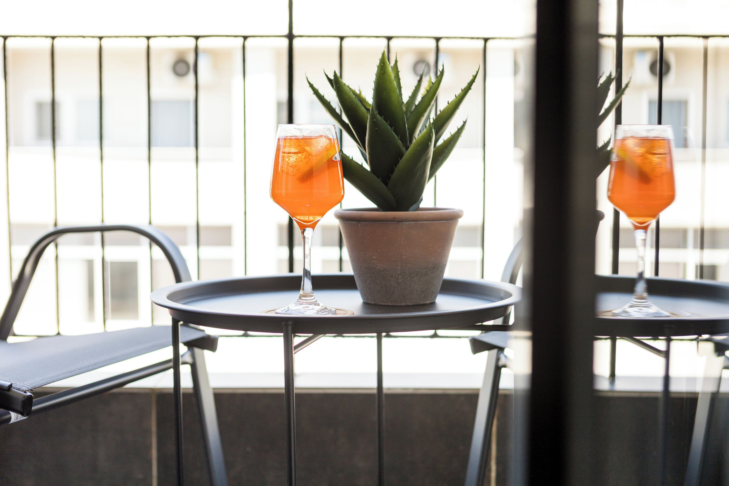 A balcony with two chairs, a potted plant, and two glasses of orange beverage.
